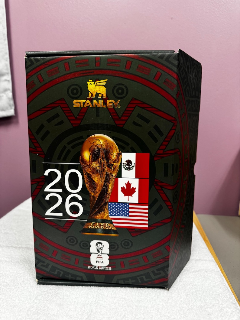 May include: A rectangular Stanley brand product box featuring a black and red graphic design. The box displays the FIFA World Cup 2026 trophy, the text 20 26, the FIFA World Cup 2026 logo, and the national flags of Mexico, Canada, and the United States.