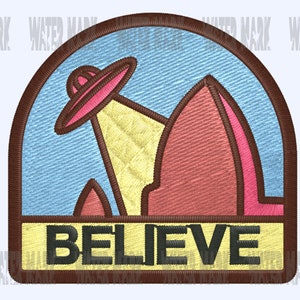 May include: A brown and yellow embroidered patch with a pink UFO flying over a red mountain range. The patch has the word "BELIEVE" written in black letters on a yellow background.