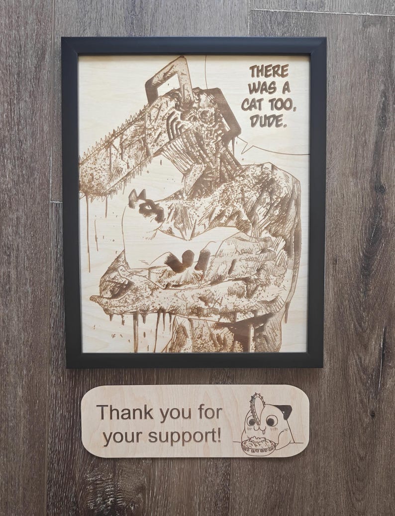 May include: Wooden framed artwork with a detailed laser-etched illustration of a chainsaw-wielding character and a cat. The text "THERE WAS A CAT TOO, DUDE." is visible. A small wooden sign below reads "Thank you for your support!"