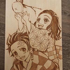 May include: A wood-burned artwork featuring two anime characters. One character is holding up their hands towards a round object. The other character is smiling. The artwork is on a light-colored wooden surface.