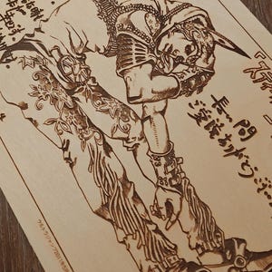 May include: A wood-burned artwork featuring a detailed illustration of a figure in a dynamic pose. The artwork includes Japanese text and intricate patterns, showcasing a character from a manga or anime series. The piece is on a light-colored wooden surface.