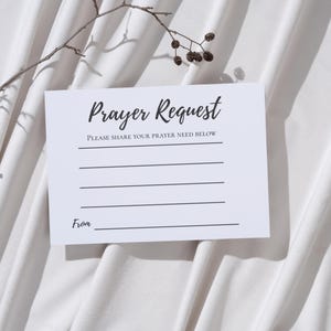 Pode incluir: Um cartão branco com as palavras "Prayer Request" em escrita elegante. O cartão tem linhas para escrever e o texto "Please share your prayer need below". Um galho de planta está no fundo.