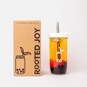 May include: A 700 ml reusable bubble tea cup with a straw and a brown cardboard box with the text "Rooted Joy" and a graphic of a jar with boba. The cup is filled with a layered drink of yellow, red, and black boba.