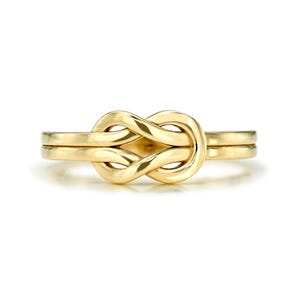 Könnte beinhalten: Ein goldener Knotenring mit einem schlichten, eleganten Design. Der Ring besteht aus einem einzigen Stück Metall, und der Knoten ist glatt und poliert.