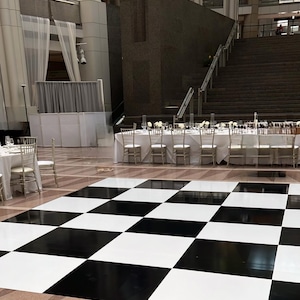 May include: A black and white checkered dance floor in a large, modern building with white walls and a staircase in the background.