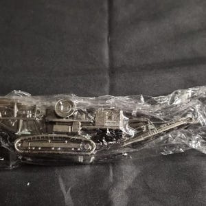 Op de afbeelding: Een zilverkleurig miniatuur tankmodel, verpakt in helder plastic. De tank heeft gedetailleerde rupsbanden, een geschutskoepel en andere componenten, wat wijst op een militair of historisch thema. Het model is waarschijnlijk een verzamelobject of een speelgoed.