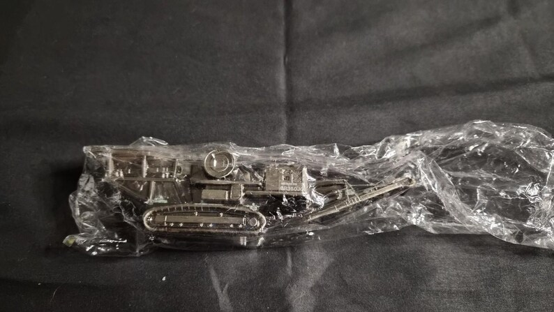 Op de afbeelding: Een zilverkleurig miniatuur tankmodel, verpakt in helder plastic. De tank heeft gedetailleerde rupsbanden, een geschutskoepel en andere componenten, wat wijst op een militair of historisch thema. Het model is waarschijnlijk een verzamelobject of een speelgoed.