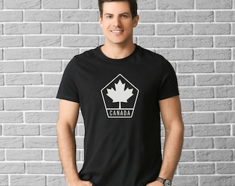 Pode incluir: Uma camiseta preta com um gráfico branco de uma folha de bordo dentro de um pentágono com a palavra "CANADA" abaixo.