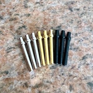 May include: A set of ten metal watch band pins in three colors: silver, gold, and black. The pins are arranged in a semi-circle on a brown granite surface.