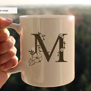 May include: White ceramic mug with a brown floral design featuring the letter "M".