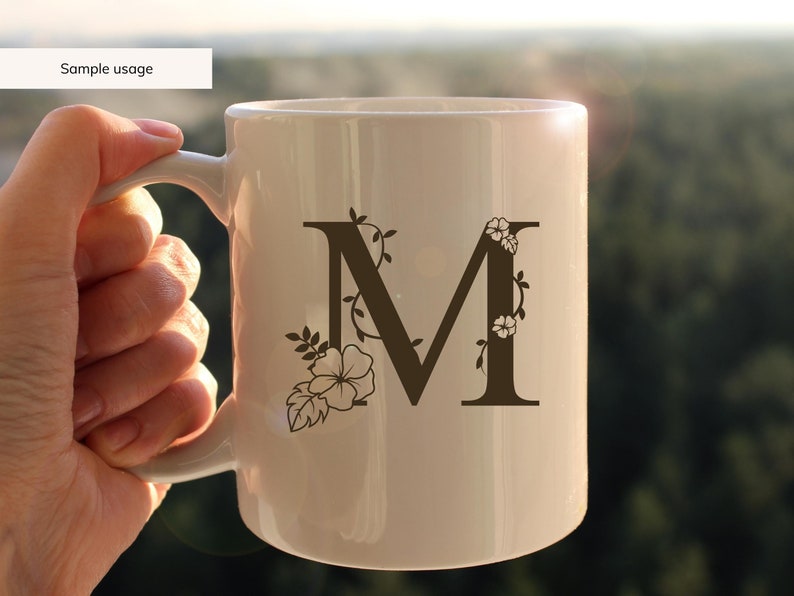 May include: White ceramic mug with a brown floral design featuring the letter "M".