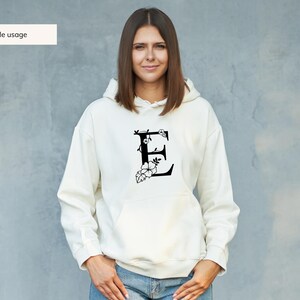 May include: A white hoodie with a black floral design featuring the letter "E" on the front.