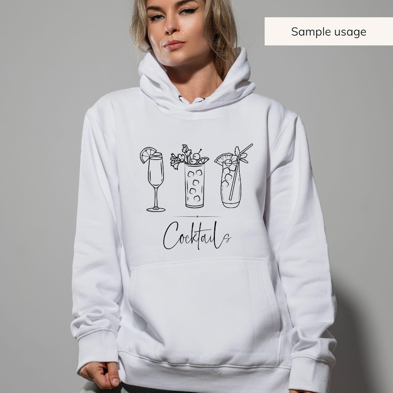 May include: White hoodie featuring a black line drawing of three cocktails with garnishes. The word "Cocktails" is written in a cursive font below the drawings. The phrase "Sample usage" is in a white rectangle in the upper right corner.