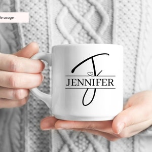 Peut inclure: Une tasse en c&eacute;ramique blanche avec un motif noir et blanc. Le motif repr&eacute;sente une lettre stylis&eacute;e "J" avec un petit c&oelig;ur et le nom "JENNIFER" imprim&eacute; en dessous.