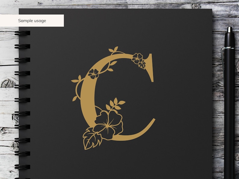 May include: A gold letter C with floral embellishments. The letter is on a black background.