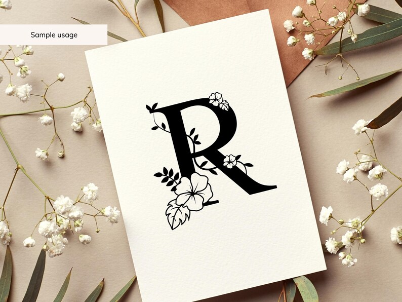 May include: A black floral monogram letter R with white flowers and leaves. The letter is on a white background.