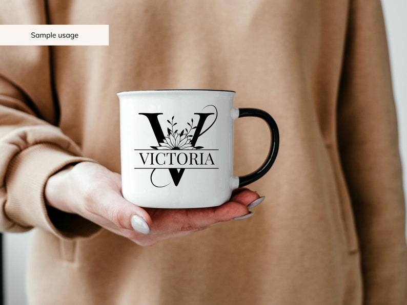 May include: White ceramic mug with a black handle. The mug has a black floral design with the letter "V" and the name "VICTORIA" printed on it.