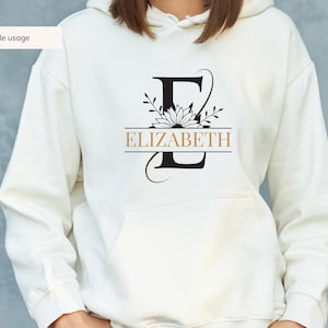 May include: White hoodie with a black floral design and the name "ELIZABETH" printed in gold.
