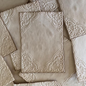 May include: A collection of cream-colored stationery with embossed floral and scrollwork designs. The paper has a textured appearance, with various sizes of cards and corner pieces. The embossed details create a raised, three-dimensional effect.