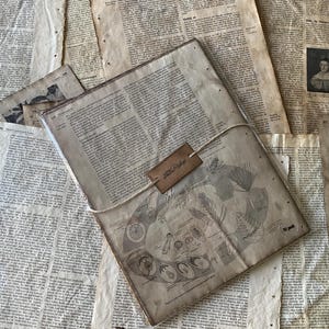 Peut inclure: Un journal de style vintage avec une illustration botanique et une étiquette en cuir attachée avec de la ficelle, posé sur un fond de papier vieilli. Les pages du journal présentent du texte imprimé et des schémas. L'étiquette indique "Love Vintage".