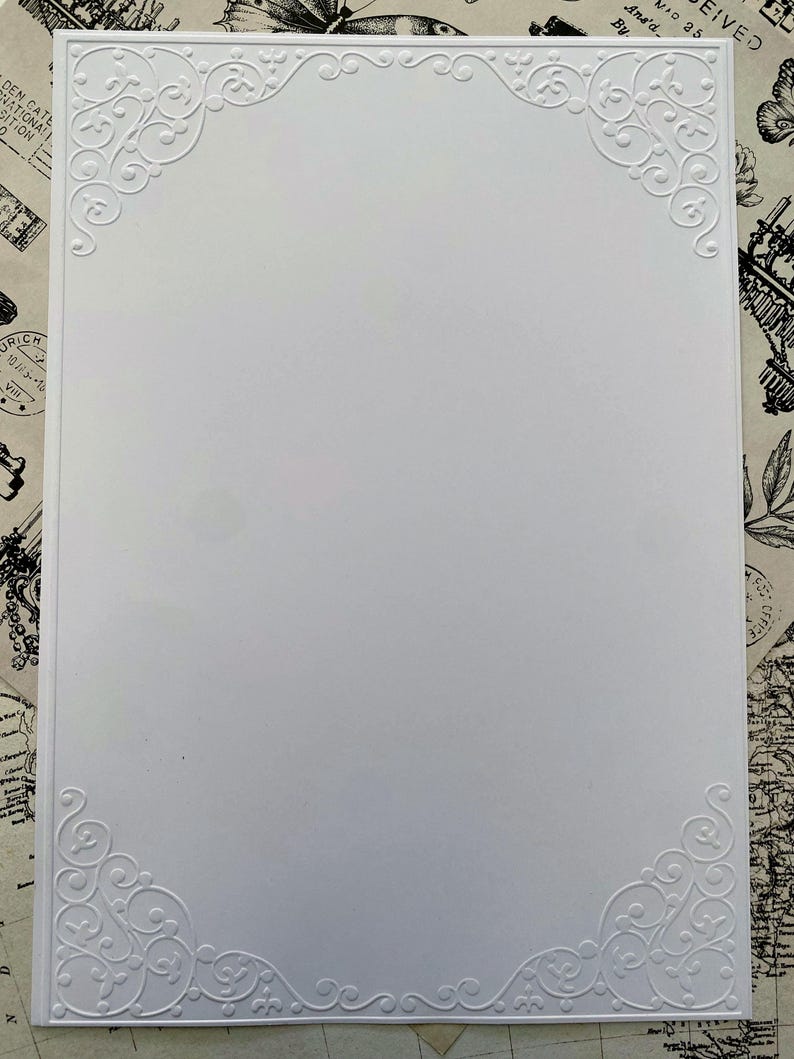 K&ouml;nnte beinhalten: Eine wei&szlig;e rechteckige Karte mit gepr&auml;gten floralen Eckendesigns. Die Karte hat eine saubere, minimalistische &Auml;sthetik mit komplizierten, wirbelnden Mustern in jeder Ecke. Der Hintergrund ist eine Vintage-Karte.