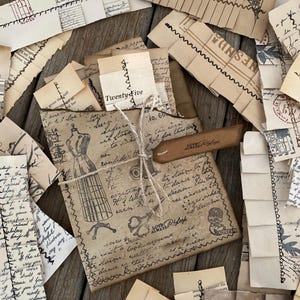 May include: A collection of vintage paper ephemera, including envelopes, tags, and torn paper scraps. The items are in shades of beige and brown, with handwritten text, illustrations, and decorative stitching. A tag reads "Love Always".
