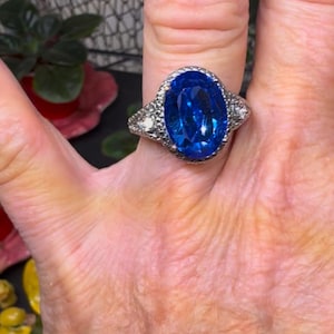 Puede incluir: Un anillo de plata con una gran piedra preciosa ovalada azul rodeada de pequeñas piedras preciosas transparentes.