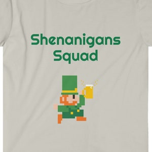 May include: A light gray t-shirt with the text "Shenanigans Squad" in green. A pixelated image of a leprechaun holding a beer mug is below the text.