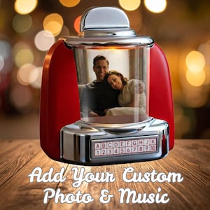 Op de afbeelding: Een rode en chromen fotolijst in jukebox-stijl met een foto van een stel erin. De lijst heeft een retro-ontwerp met een selectiepaneel en de tekst "Add Your Custom Photo & Music".