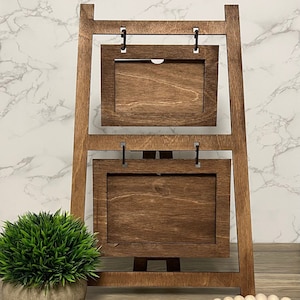 May include: A wooden easel with two picture frames. The easel is brown and has a rustic look. The frames are also brown and have a simple design.