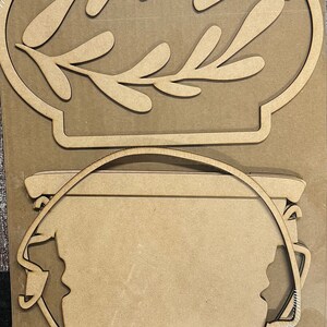 May include: A wooden craft kit with two pieces: a bucket with a handle and a separate piece with a leafy design. The pieces are unfinished and ready to be painted or stained.