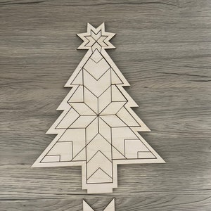 May include: A wooden Christmas tree ornament with a geometric design. The tree is made of multiple pieces that fit together. The ornament is unfinished and ready to be painted or stained.