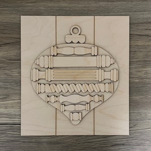 May include: A wooden ornament shaped like a Christmas tree ornament with a variety of decorative elements, including a rope design, a star, and a loop at the top.