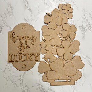 May include: A wooden craft kit featuring a sign that says "happy go lucky" and a set of shamrock shapes. The shamrocks are designed to be layered to create a 3D effect.