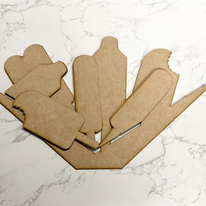 May include: A set of seven wooden popsicle shapes, each with a bite taken out of the top. The shapes are arranged in a fan pattern on a white marble surface.