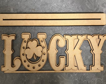 May include: Wooden sign with the word "LUCKY" in large, stylized letters. The "U" is replaced with a horseshoe and a shamrock.