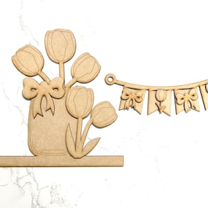 May include: Wooden craft kit featuring a vase with tulips and a banner with tulips and bows. The vase and banner are unfinished and ready to be painted.