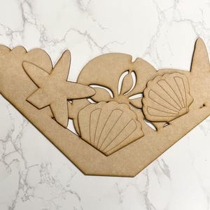 May include: Wooden cutout of a seashell, starfish, and sand dollar. The cutout is in the shape of a basket.
