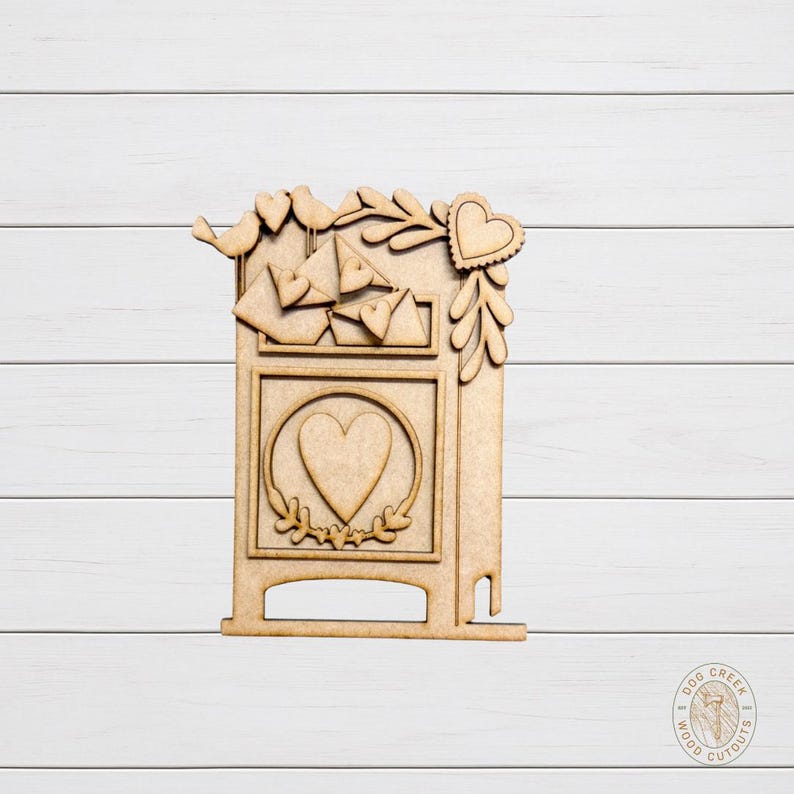May include: A wooden cutout of a mailbox with a heart-shaped design. The mailbox features a large heart in the center, smaller hearts, birds, and decorative leaves. The cutout is made of light brown wood.