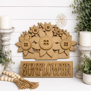 May include: A light brown wooden cutout featuring a cluster of sunflowers with button centers, positioned above a rectangular wooden sign with the word SUNFLOWER in raised lettering. The design includes a circular logo with the text DOG CREEK WOOD CUTOUTS.