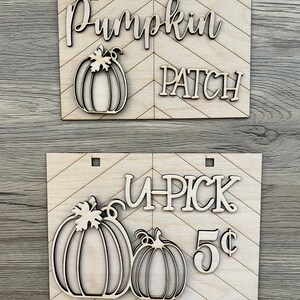 May include: Two wooden signs with a chevron pattern. The top sign says "Pumpkin Patch" with a pumpkin cutout. The bottom sign says "U-Pick 5¢" with two pumpkin cutouts.
