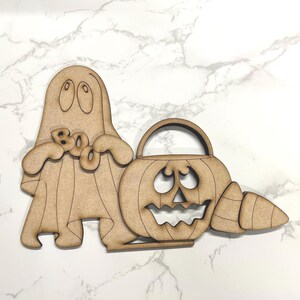May include: Wooden cutout of a ghost holding a "BOO" sign and a pumpkin with a candy corn. The pumpkin has a jack-o'-lantern face and a handle.