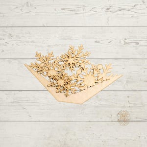 May include: A wooden snowflake-themed decoration. The piece features several laser-cut snowflakes arranged within a triangular frame. The natural wood color provides a neutral base for seasonal crafts or decor. The design is suitable for winter or holiday themes.
