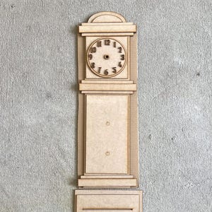 May include: A wooden miniature grandfather clock with a clock face showing the numbers. The clock is made of light brown wood and has a rectangular shape with a base and a decorative top.