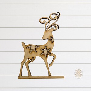 May include: A wooden reindeer cutout with snowflake cutouts and decorative antlers. The reindeer is standing on a base and is made of light brown wood. The background is white.