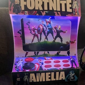 Puede incluir: Un expositor de cartón con la palabra "FORTNITE" en la parte superior. El expositor muestra varios personajes del juego, incluido el Capitán América. El nombre "AMELIA" está impreso en la parte inferior.