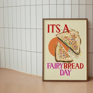 May include: A framed poster with a white background and a colorful illustration of two slices of fairy bread. The text "IT'S A FAIRY BREAD DAY" is printed in red and pink letters.