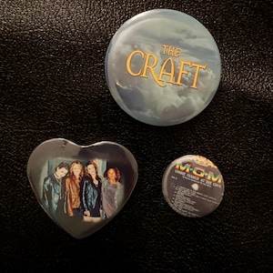 May include: A circular pinback button featuring the text THE CRAFT in gold, a heart-shaped pinback button displaying a group of four people, and a small circular pinback button showing the MGM logo and the text CONNIE FRANCIS AT THE COPA.