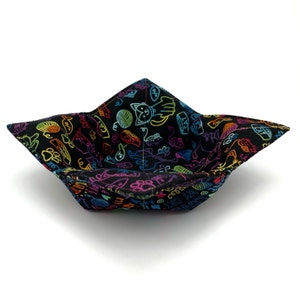 May include: A black fabric bowl with a colorful cat-themed print. The bowl is folded and has a star-shaped bottom.
