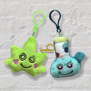 May include: Two plush keychains: a green star with spiral eyes and pink hearts, and a blue bong with a smiling face. Both have attached clips. The brand name "Sunshine Be-Stitched" is visible.